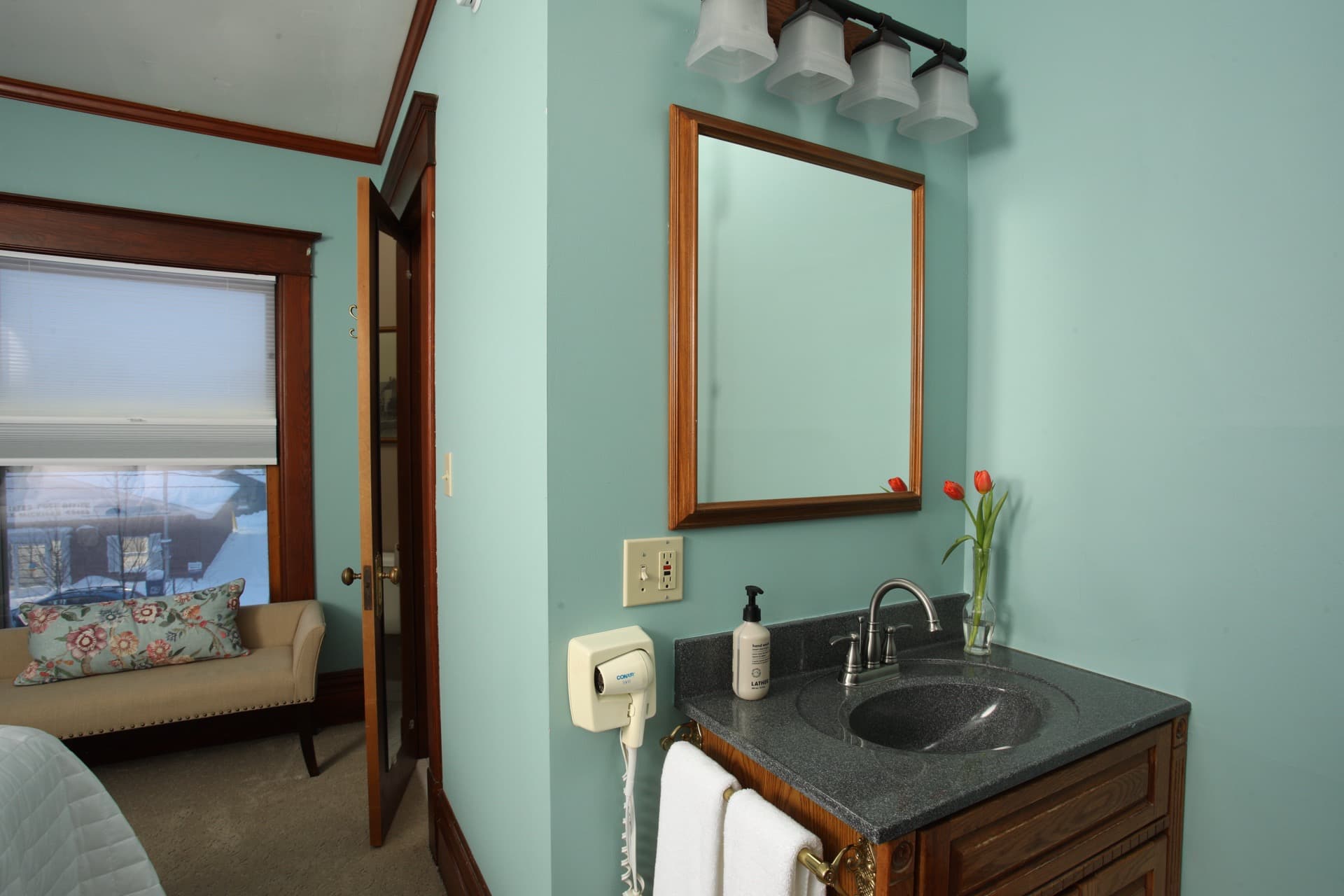 Bathroom with gray walls, two towels on a brass rack, and a view into an adjacent room.