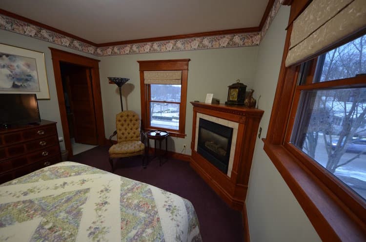 Bedroom with light pink walls, a bed with a white comforter, a fireplace, and two windows.