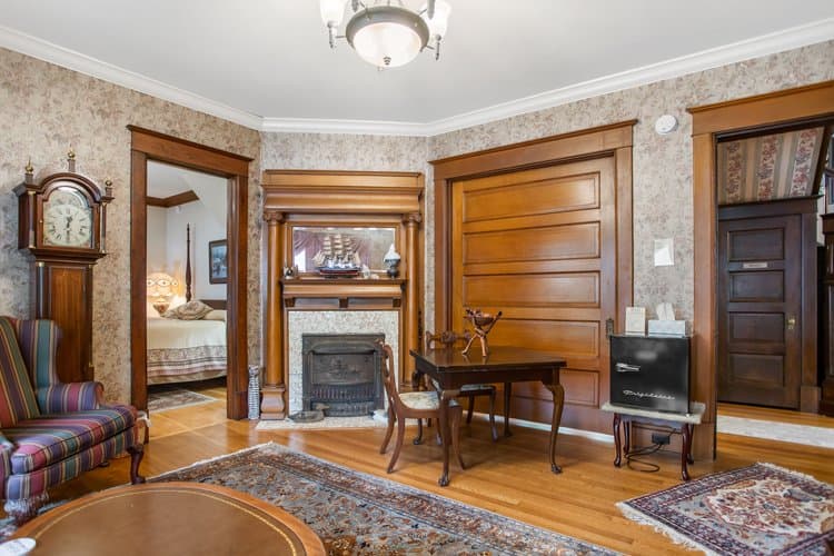 Interior room with wood trim, patterned wallpaper, fireplace, and antique furniture.