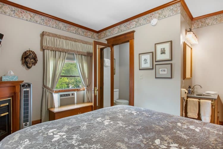 Bedroom with a patterned comforter, fireplace, and open doorway to a bathroom.