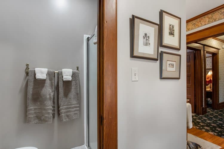 Bathroom with gray walls, two towels on a brass rack, and a view into an adjacent room.