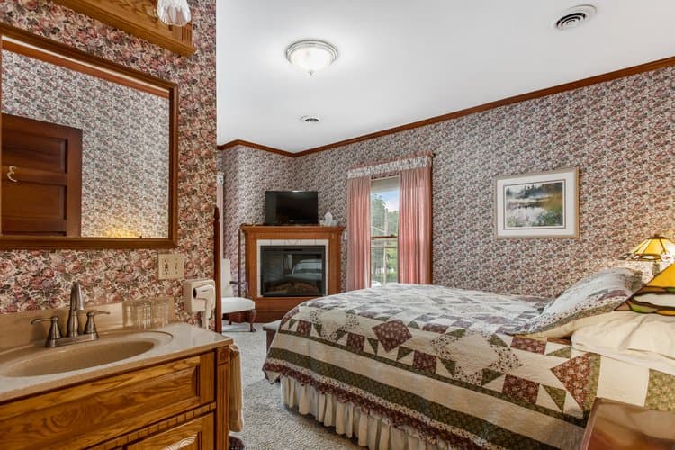 Bedroom with floral wallpaper, a bed with a quilt, a fireplace, and a sink vanity.