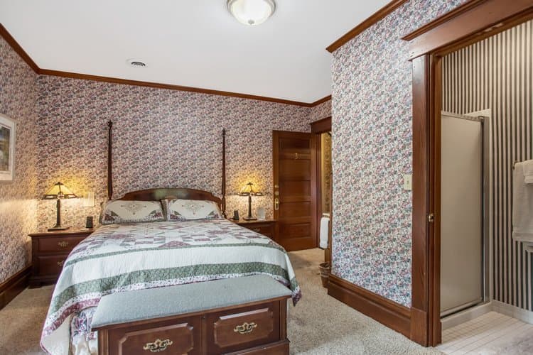 Bedroom with floral wallpaper, a four-poster bed, and an open doorway to a bathroom.