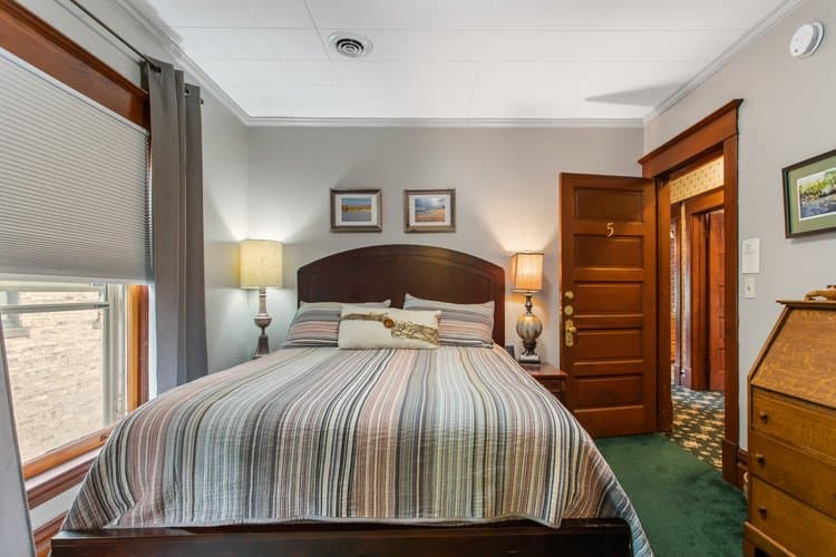 Bedroom with a striped comforter, two bedside lamps, and a wooden door leading to another room.