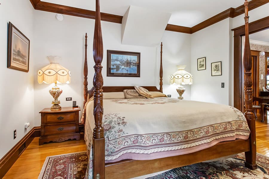 A cozy bedroom featuring a four-poster bed, decorative lamps, and framed artwork.