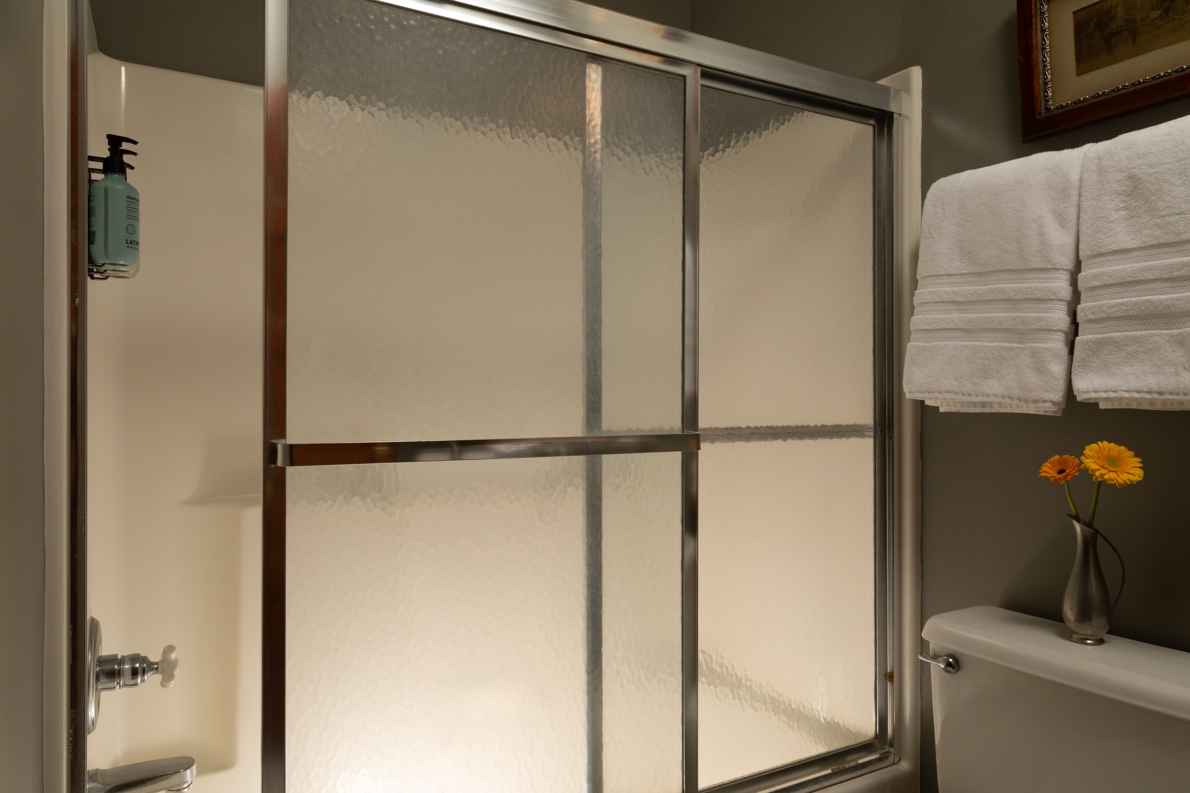 A shower stall with glass doors, neatly arranged towels, and a small vase with flowers on the side.