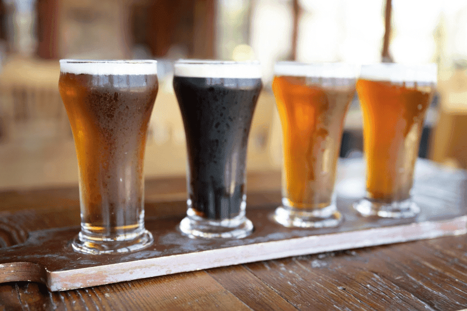A flight of four different craft beers sits on a wooden tray.
