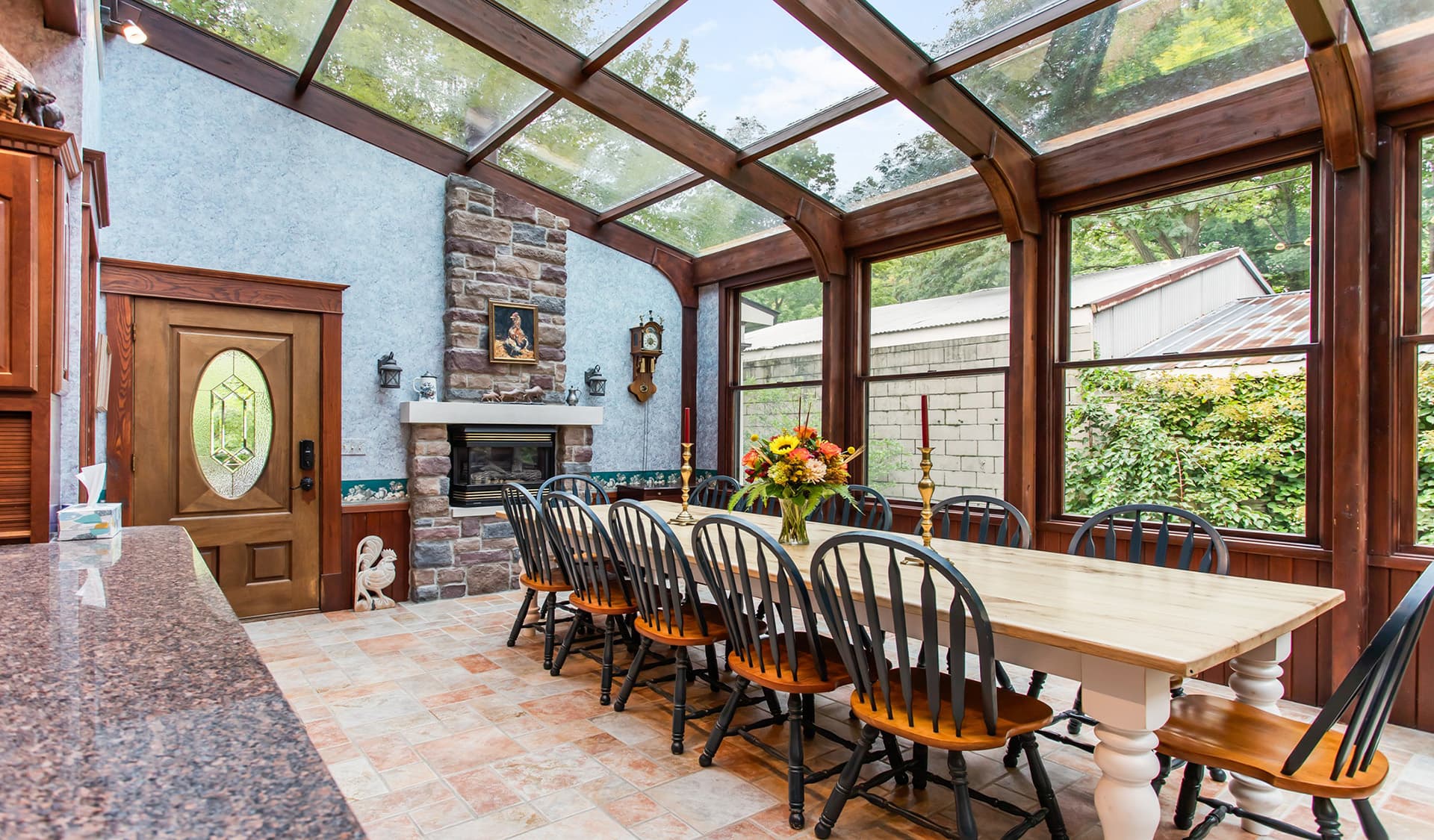 Bright and inviting sunroom featuring a large dining table, stone fireplace, and panoramic windows.